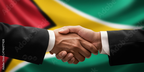 Businessman and diplomat in suits clasp hands for handshake over Guyana flag, agree on united success in trade, diplomacy, cooperation, negotiation, support, teamwork in commerce, gesture of greeting photo