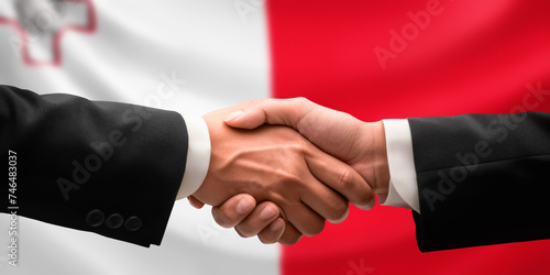 Businessman and diplomat in suits clasp hands for handshake over Malta flag, agree on united success in trade, diplomacy, cooperation, negotiation, support, teamwork in commerce, gesture of greeting