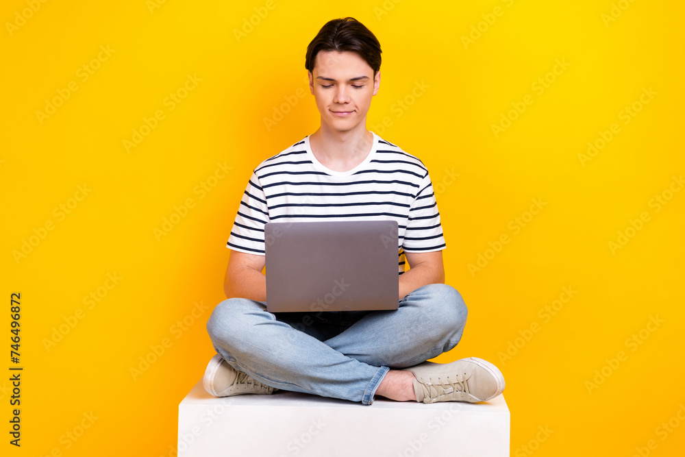Photo of positive cute guy dressed striped t-shirt working modern device isolated yellow color background