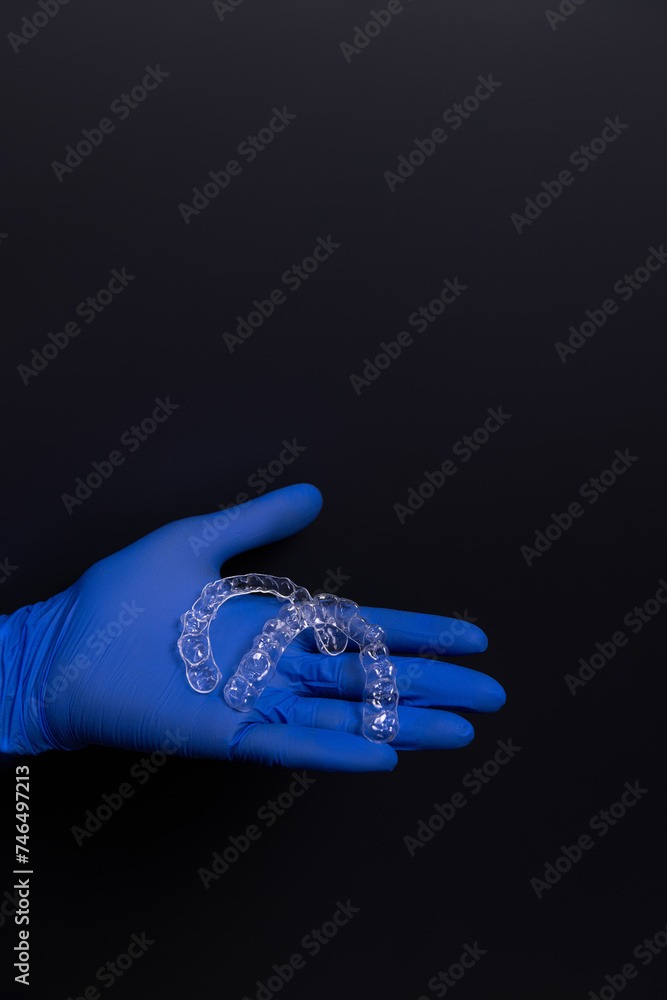 A dentist in blue rubber gloves holds transparent plastic aligners, which are devices used to correct bite alignment in adult patients at the dental clinic in the hospital. A dentist in blue rubber gloves holds transparent plastic aligners, which are devices used to correct bite alignment in adult patients at the dental clinic in the hospital.