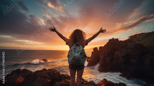 woman with backpack with raised arms relaxing at sunset while traveling, traveler enjoying freedom among serene natural landscape