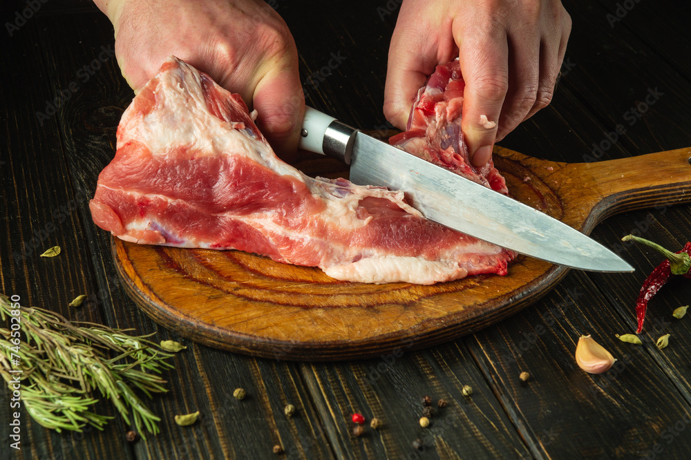 A cook cuts raw meat with a knife on a cutting board before preparing a meat dish. Recipe idea for a hotel or restaurant