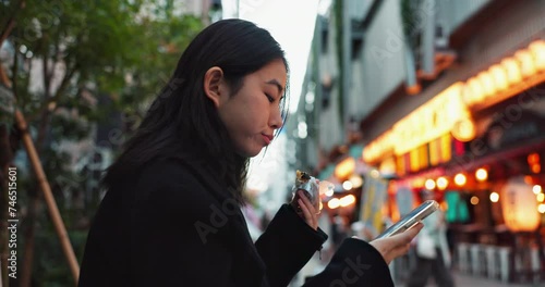 Phone, eating and Japanese woman with onigiri in Tokyo city on exploring vacation, adventure or holiday. Hungry, food and young female person enjoying an Asian snack or meal in town on weekend trip. photo