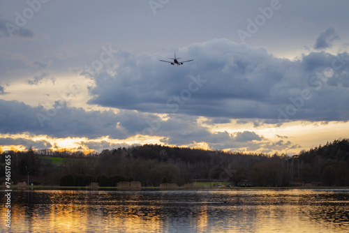 Samolot lecący nad zbiornikiem wodnym / jeziorem na tle zachodzącego słońca | The flying plane above the reservoir / lake on the sunset background
