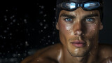 Close-up of a determined male swimmer wearing goggles, intense gaze with water droplets on his face.