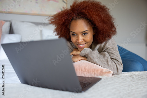 Young adult woman streaming entertainment on her laptop computer lying on her bed photo