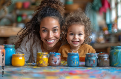 Mother and daughter smile at the camera while painting jars.