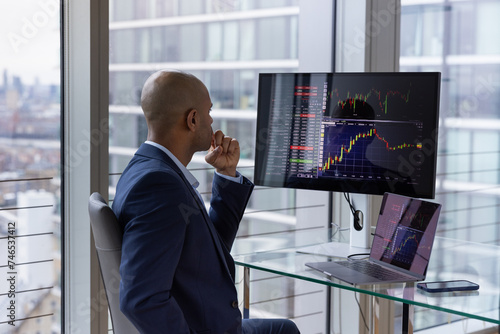 Stock trader looking at stocks and shares on computer in a high rise office photo