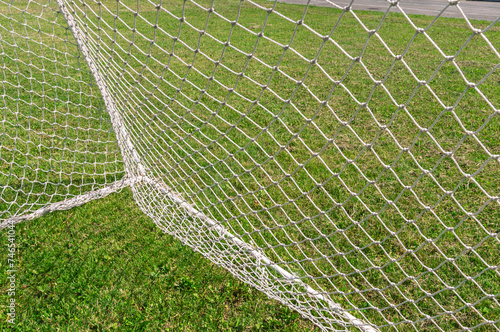 A woven net on a football goal. A football field with natural green grass. Playing football. A football field in summer.