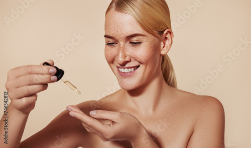 Cheerful blond woman holding a pipette with liquid serum. Smiling female with freckled skin testing serum consistency with fingers before applying.