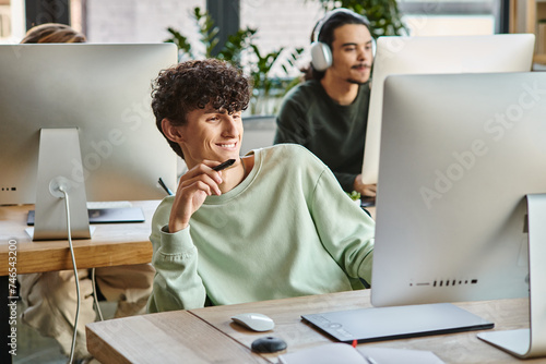 happy curly man engaged in retouching work with stylus pen in hand looking at monitor