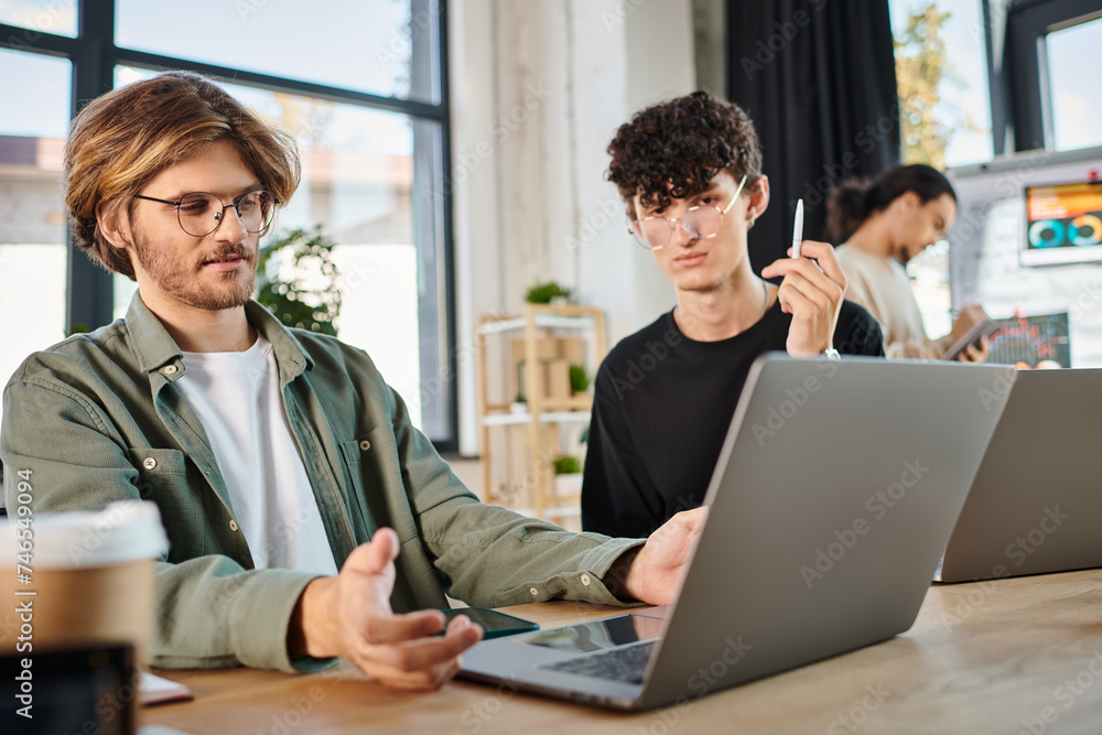Obraz premium Young startup team deeply focused while working on laptops in modern coworking space, men in 20s