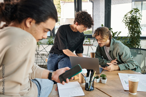 Young professionals brainstorming over a laptop in modern office near blurred coworker with phone