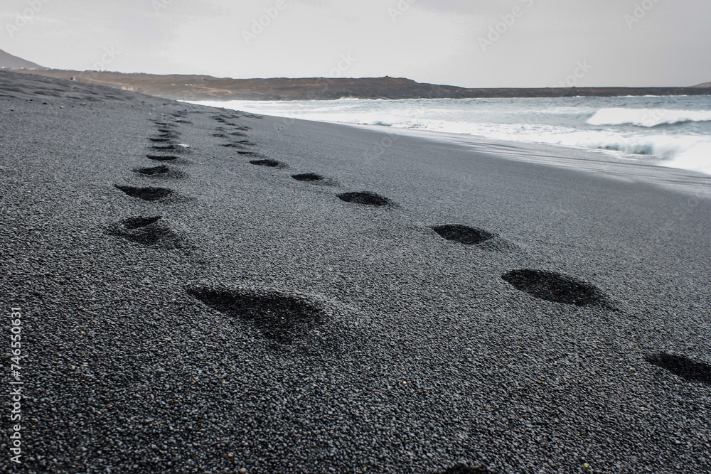 impronte sulla sabbia nera del vulcano dell'oceano  - obrazy, fototapety, plakaty 