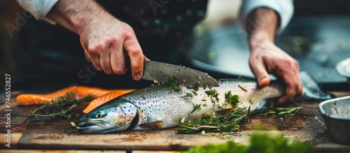 A person is skillfully cutting up a large trout on a wooden cutting board with a sharp knife. The fish is being filleted into pieces for cooking. photo