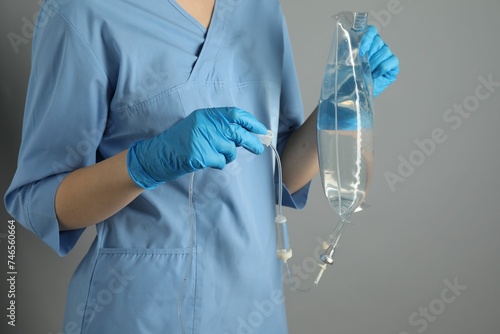 Nurse with IV infusion set on grey background, closeup photo