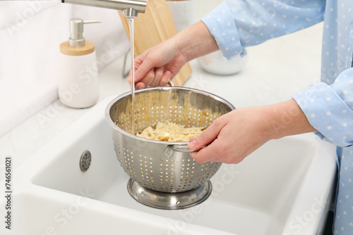 Woman rinsing pasta in colander above sink, closeup