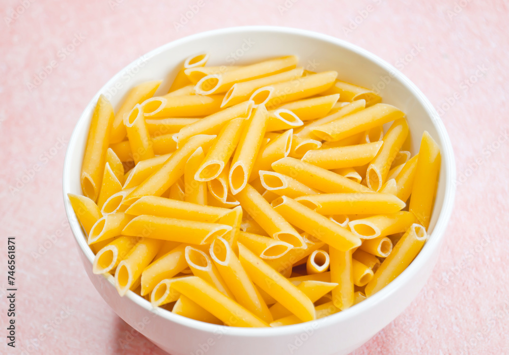 Tazón lleno de pasta cruda sobre fondo rosa Tazón lleno de pasta cruda sobre fondo rosa