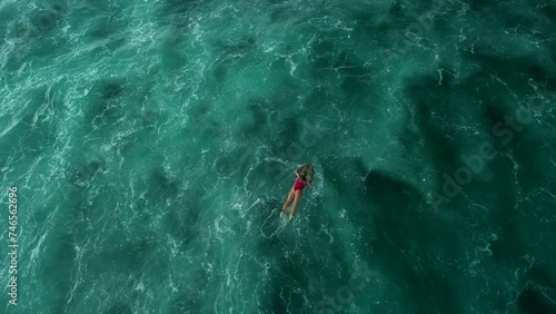 Background video of an aerial view of the ocean in which a surfer is swimming on a board. A young sexy woman in a red swimsuit rows on a line-up while lying on a surfboard. Surfing on high waves. photo
