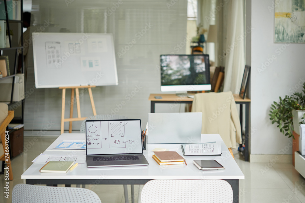 Office of small startup company with laptops and planner on desks Office of small startup company with laptops and planner on desks