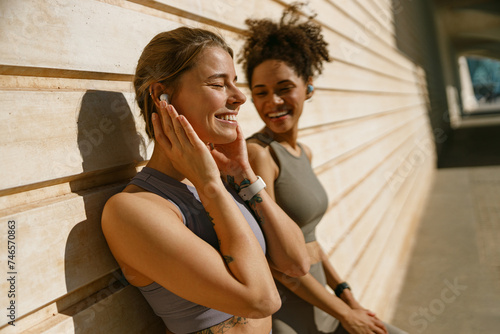 Two young female sportswomen have a rest after morning jogging outdoors and listen music
