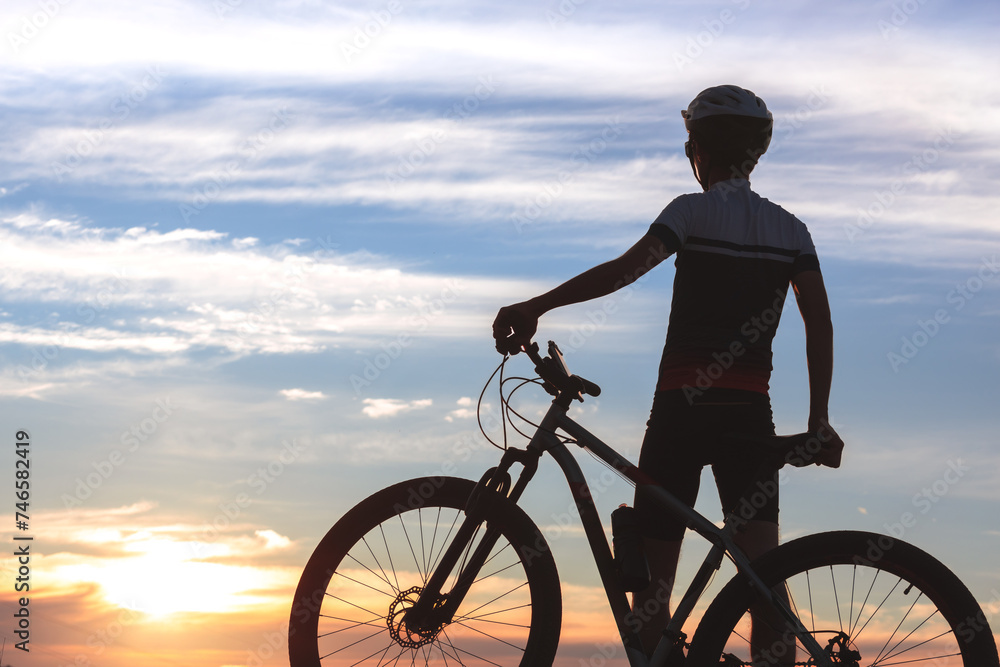 Obraz premium Silhouette of a cyclist next to his bike, standing still while admiring the sky and sunset in the background