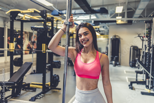 Portrait of young woman holding barbell while exercising in gym gym. Self-motivation, keep the body in good shape, athletic endurance, heavy weight training.