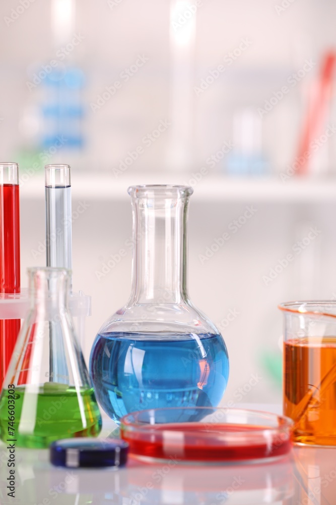 Laboratory analysis. Glass flasks and Petri dish with liquids on white table against blurred background Laboratory analysis. Glass flasks and Petri dish with liquids on white table against blurred background