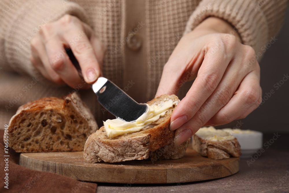 Woman spreading butter onto bread at wooden table, closeup