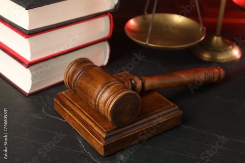 Wooden gavel, scales and stack of books on dark textured table, closeup
