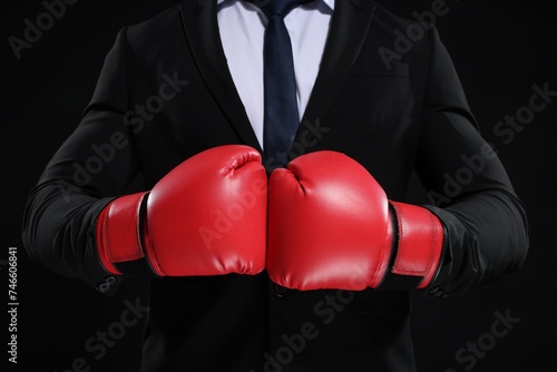 Businessman in suit wearing boxing gloves on black background, closeup © New Africa