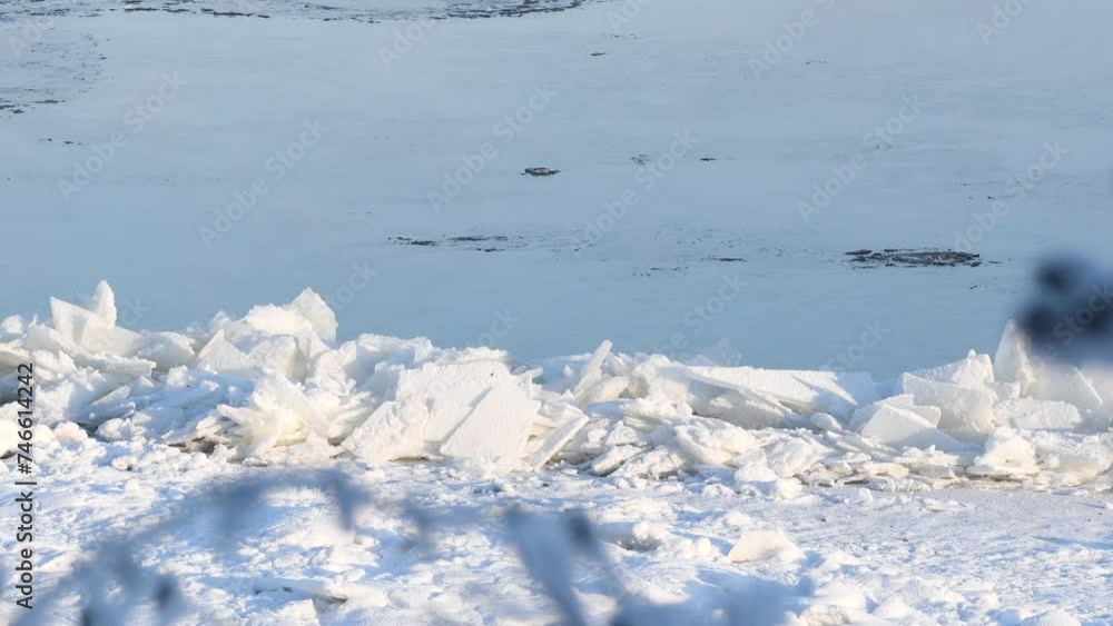 A frozen river bank with fragments of ice floes with blurred branches in the foreground A frozen river bank with fragments of ice floes with blurred branches in the foreground