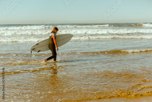 Female surfer in wetsuit with his surfboard entering out of sea after surfing on waves