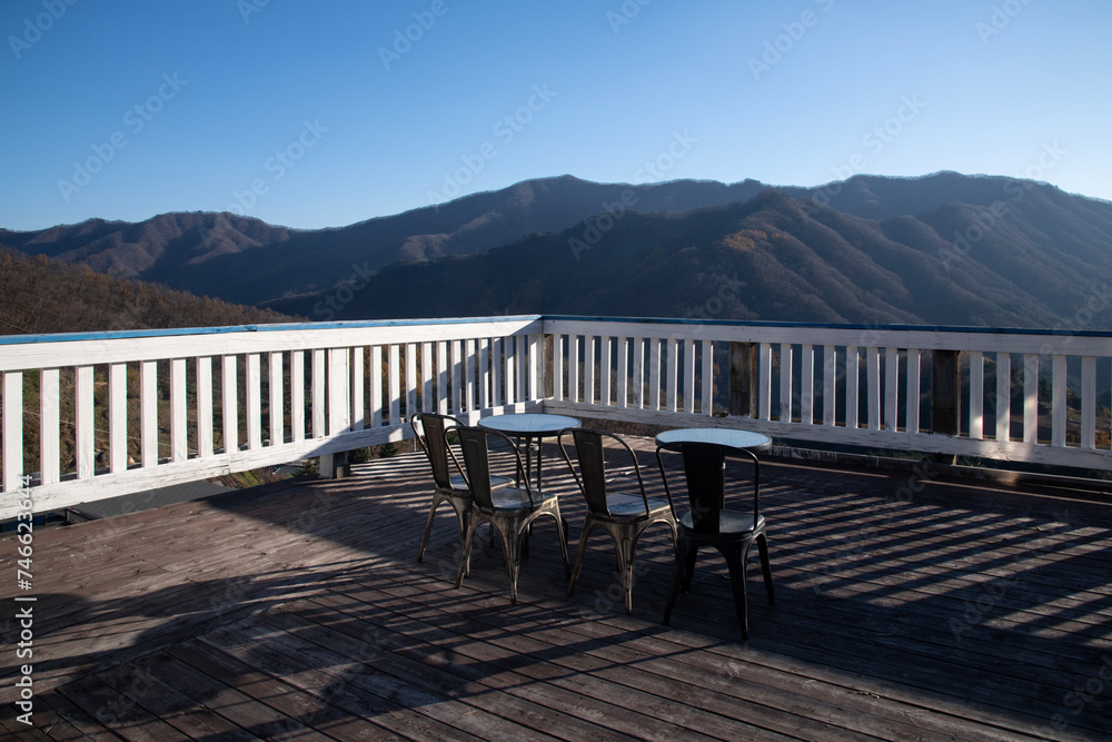 View of the wooden floor and fence with tables and chairs in the autumn mountain