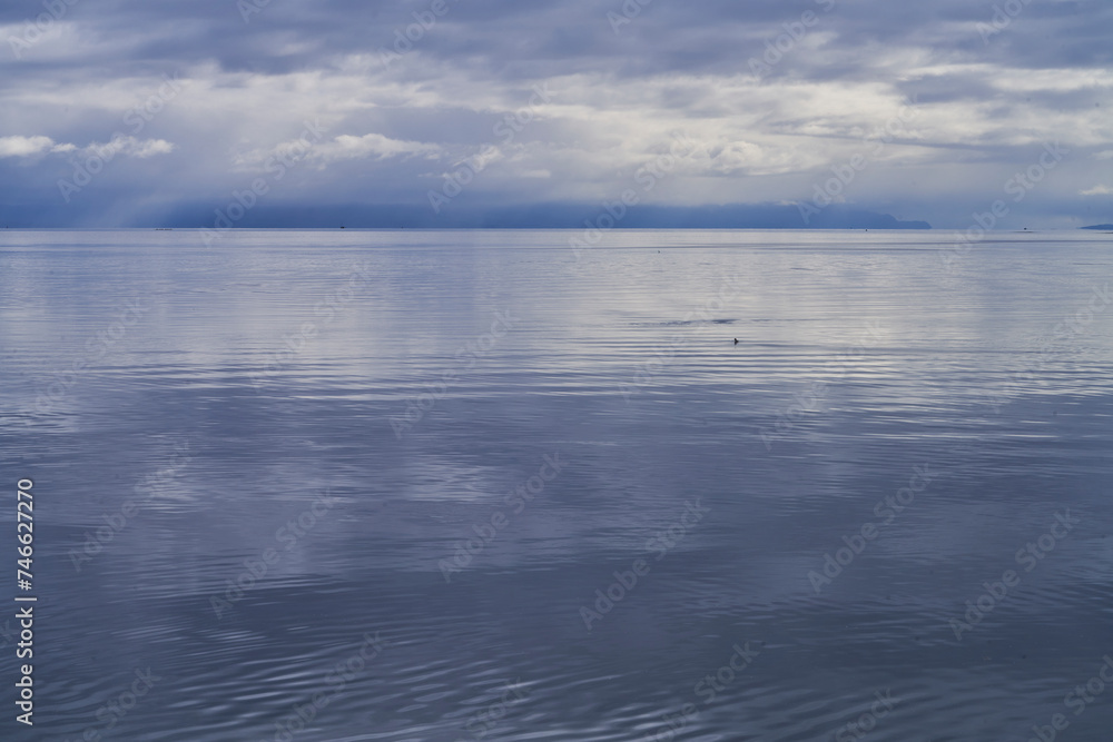 Minimalist view of an approaching rainstorm over a calm blue ocean with distant clouds and mountains