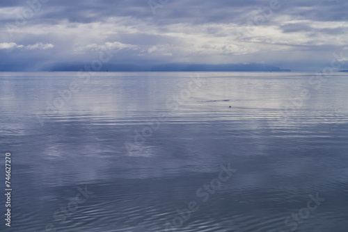 Minimalist view of an approaching rainstorm over a calm blue ocean with distant clouds and mountains