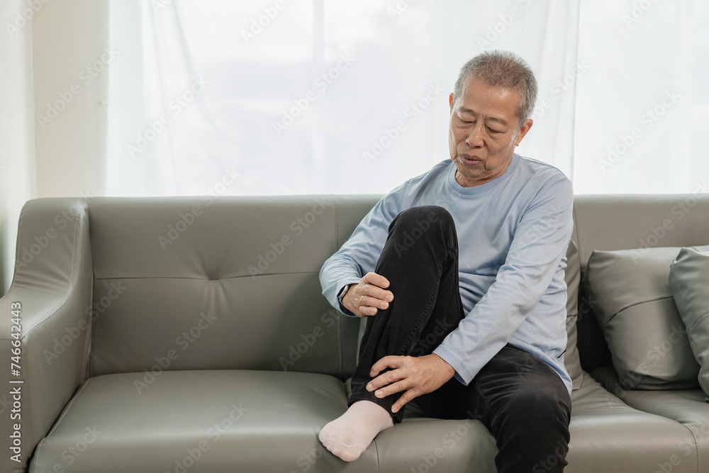 Old Asian man with knee and leg joint pain on the sofa pain in the elderly Caring for the health of the elderly Old Asian man with knee and leg joint pain on the sofa pain in the elderly Caring for the health of the elderly