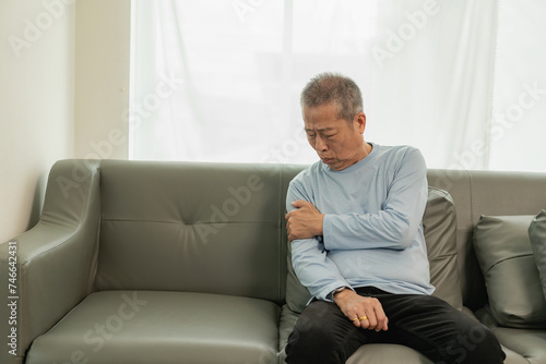 An elderly Asian male patient suffers from pain and numbness in his hand from rheumatoid arthritis. Elderly man massaging hand with pain in wrist health problems concept