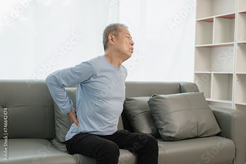Asian elderly man has back pain and sickness in bed at home, unhappy elderly man touching his back seriously and trying, elderly care concept