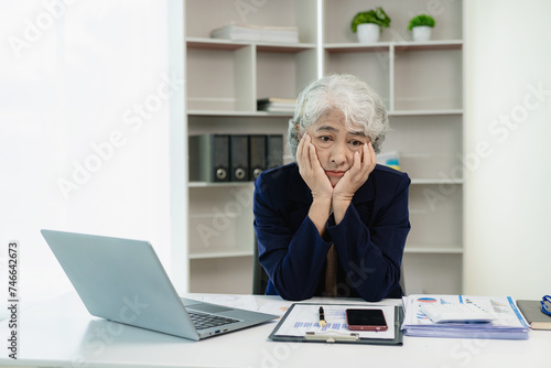 Senior Asian businesswoman thinking hard with paperwork, financial graphs and laptop, finance business concept photo