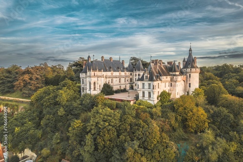 A breathtaking aerial view showcases a magnificent castle nestled amidst a dense forest  surrounded by a sea of verdant trees creating a picturesque scene of tranquility and grandeur.