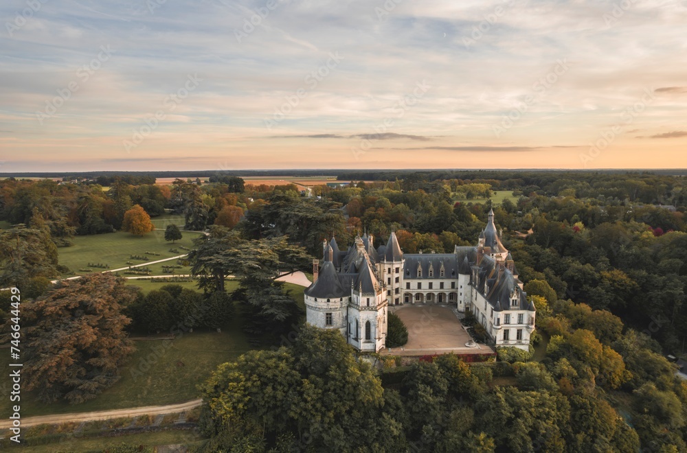 A stunning aerial perspective captures the grandeur of Chaumont-sur-Loire castle nestled among a lush forest of trees, creating a serene and enchanting scene