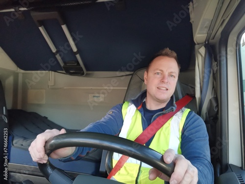 Truck Driver driving with high Visibility Vest and Red Seat Belt on, behind the Steering Wheel of a Semi Truck. interior Image. 