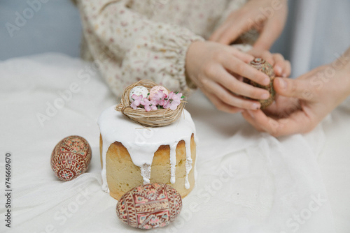 Easter cake with white glaze with a decorative bird s nest with eggs and flowers. Wooden hand painted Easter eggs in hands.