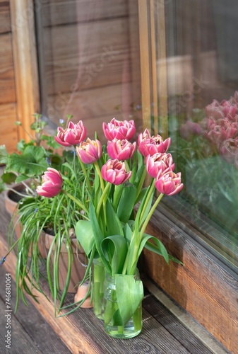 bouquet of tulips in vase and  potted in front of a bay window on wooden terrace