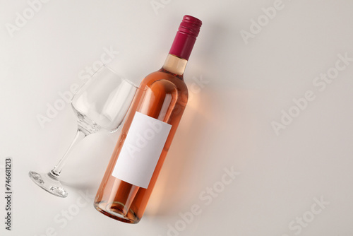 Bottle of tasty rose wine and glass on white background, flat lay. Space for text