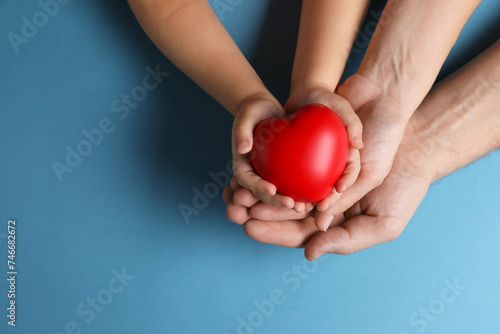 Father and his child holding red decorative heart on light blue background  top view. Space for text