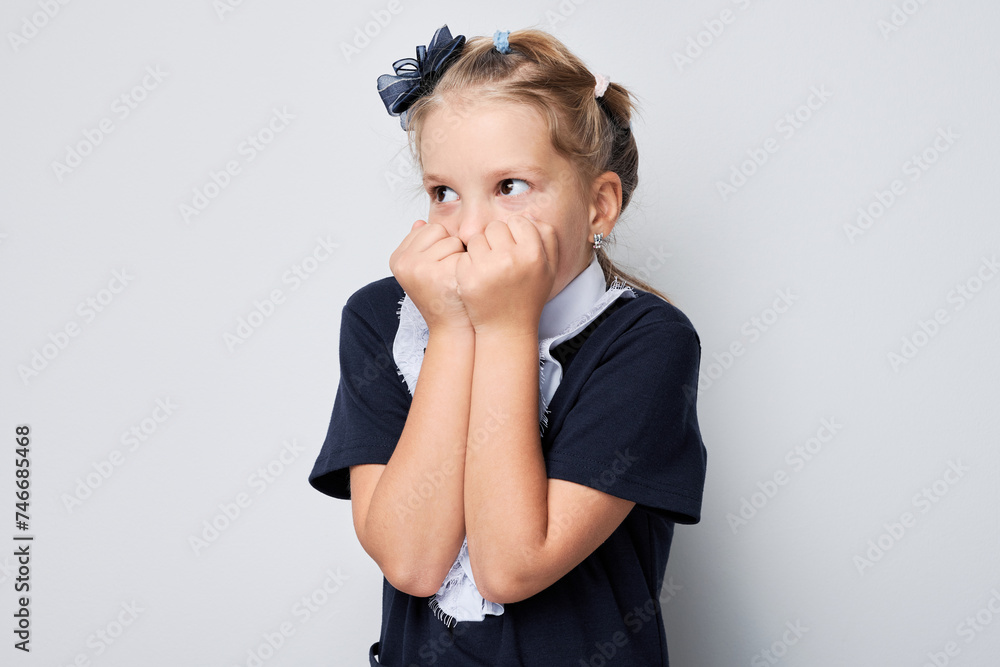 Portrait of young girl in school uniform covering mouth with hands looking away on light background Portrait of young girl in school uniform covering mouth with hands looking away on light background