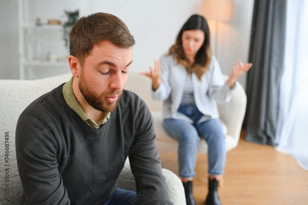 Obraz premium Couple arguing. Wife shouting to her desperate husband sitting on a couch in the living room at home