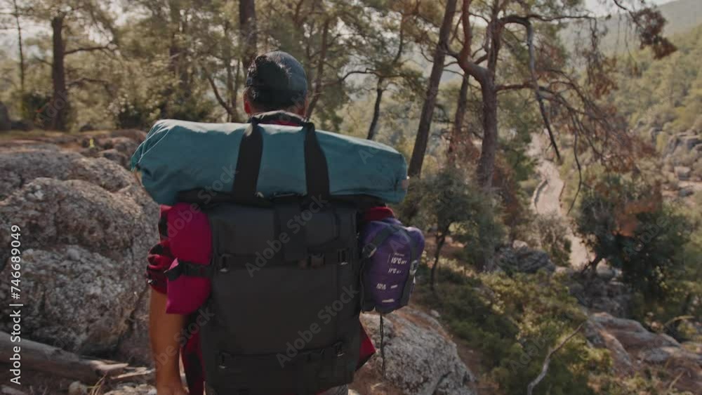 A tourist with a hiking backpack walks along a rocky path in a coniferous forest A tourist with a hiking backpack walks along a rocky path in a coniferous forest